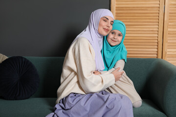 Muslim woman and her daughter sitting on sofa at home