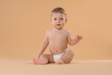 Cute little baby in diaper sitting on beige background