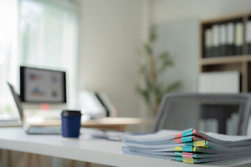 Stack of documents with colorful paper clips lying on white desk in blurred modern office interior...