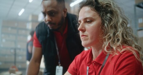 Two diverse warehouse workers or logistics specialists talking, preparing E-commerce orders for shipping to customers, using laptop computer, working in post office. Online store delivery service.