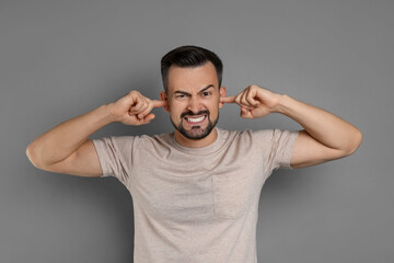 Man covering his ears with fingers on grey background