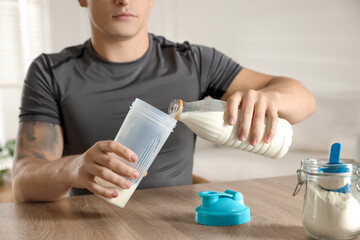 Making protein cocktail. Man pouring milk into shaker at wooden table, closeup