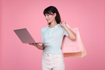 Internet shopping. Happy woman with laptop and colorful bags on pink background