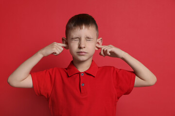 Little boy covering his ears with fingers on red background