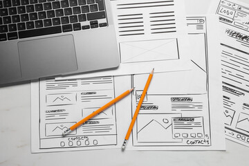 Developing UI design. Sketches of website wireframes, laptop and pencils on white marble table, top...