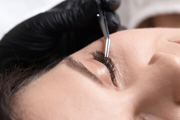 Woman undergoing lash extensions procedure in beauty salon, closeup