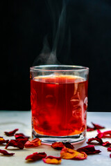 Red tea in a glass with rose petals on a black background