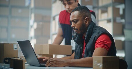 African American logistics specialist works on laptop computer in post office. Warehouse employee brings parcel to check delivery information. Sorting center of E-commerce online store. Slow motion.