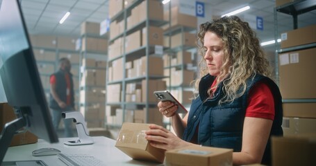 Female logistics manager scans small parcels using smartphone, works in warehouse of postal service. Sorting center employees carrying cardboard boxes for shipping to clients. E-commerce online orders