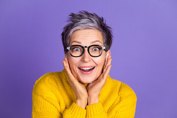 Joyful mature woman in glasses with surprised expression against purple background
