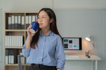 Young businesswoman sipping coffee and contemplating future projects while standing in a modern...