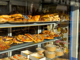 Freshly baked pastries and pizzas displayed in a bakery window during the morning hours in a lively urban setting