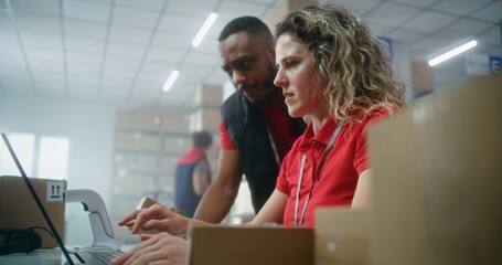 Team of multiethnic warehouse associates or inventory managers talking, preparing E-commerce orders for shipping to clients, using laptop computer. Logistics distribution center or delivery service.