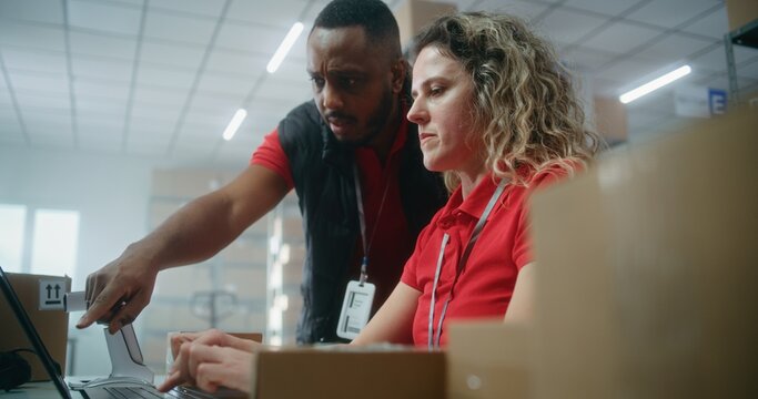 Team of multiethnic warehouse associates or inventory managers talking, preparing E-commerce orders for shipping to clients, using laptop computer. Logistics distribution center or delivery service.