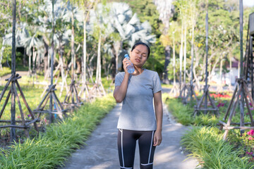 Young woman holds a water bottle against her neck to cool off on a hot day or after exercising outdoors on a park trail. Healthy living concepts. Tired from exercising outdoors.