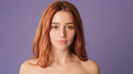Naklejka premium Close-up of red-haired woman looking at camera on purple background. Beautiful girl poses in studio with blank space on violet wall for your promotion