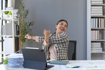 Happy businesswoman is stretching her arms while sitting at her desk in a modern office, taking a break from work and enjoying a moment of relaxation