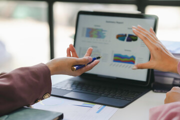 Businesswomen are analyzing financial data on a tablet screen showing charts and graphs, discussing business strategy and planning for investment