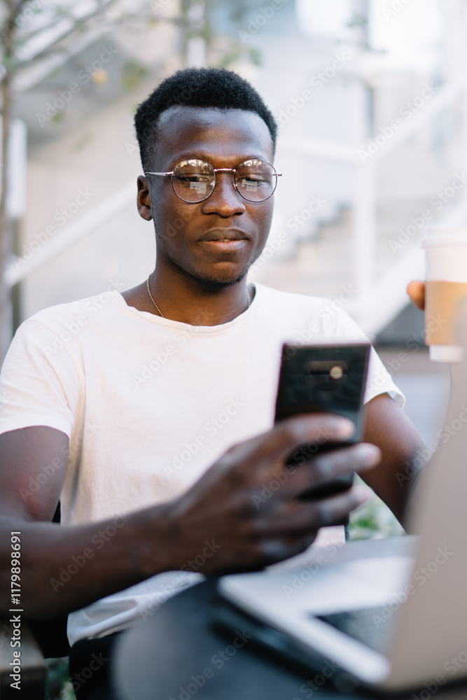 Poster pensive prosperous male freelancer sitting near laptop computer for remote job using smartphone for 