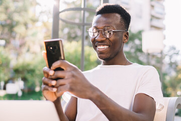 Joyful African American male using smartphone on street