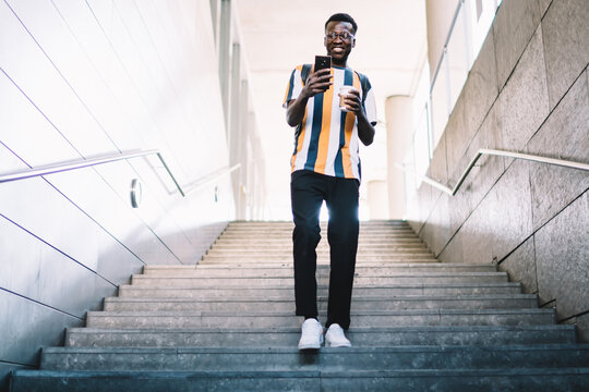 Positive black man walking downstairs and messaging on smartphone