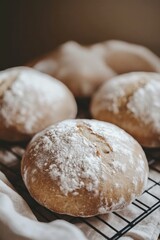Fototapeta premium Close-up view of four freshly baked artisan sourdough bread loaves, dusted with flour, resting on a cooling rack.