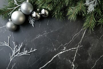 Elegant silver Christmas ornaments and frosted pine branches arranged on a dark marble background.