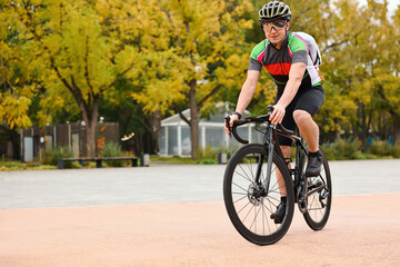 Athletic man with helmet riding bicycle outdoors, space for text
