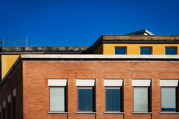 Modern Building Facade with Red Brick and Geometric Windows Against a Clear Blue Sky..
