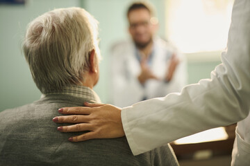 Close up of unrecognizable doctor supporting her senior patient in the office