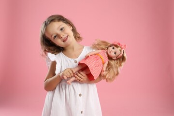 Cute little girl with doll on pink background