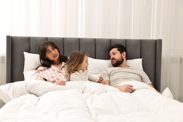 Fototapeta premium Happy playful daughter with her overwhelmed parents in bed at home