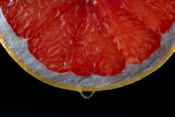 Juicy red grapefruit slice with drop on black background . Texture fresh citrus fruit, closeup, healthy sweet food. Macro photography