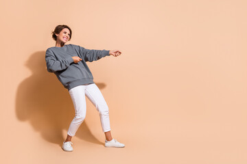 Full length photo of adorable girl wear pullover white trousers pull heavy object from empty space isolated on beige color background © deagreez