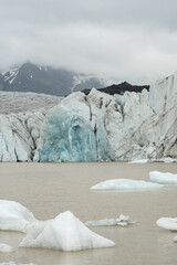 Front off a glacier in Iceland. With blue ice and black mountain in the back. Clouded weather, dark mood Icelandic scenery. Nature background. Adventure vacation.