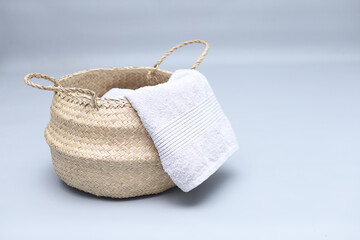 Straw wicker basket and white natural cotton towel on gray background. Fashionable bamboo basket stylish interior item eco design handmade, copyspace