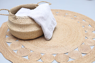 Fashionable bamboo basket with natural cotton towel on handmade jute rug. Stylish interior item. Eco design for  bathroom.Space for text.