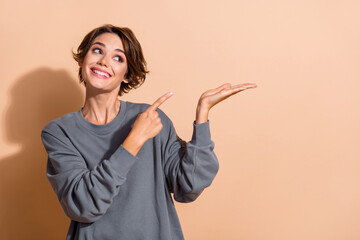 Photo portrait of pretty young girl point look palm hold empty space dressed stylish gray outfit...