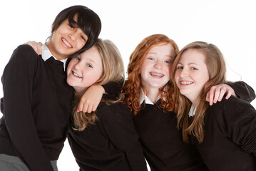 Early Teenage Students: Best Friends. A candid group of smiling teenage girl friends in their school uniforms isolated against a white background.
