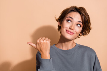 Photo portrait of pretty young girl point look empty space wear trendy gray outfit isolated on beige color background