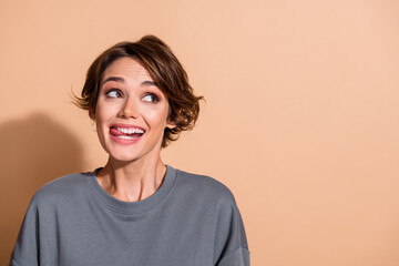 Fototapeta premium Photo portrait of pretty young girl look empty space tongue out tasty wear trendy gray outfit isolated on beige color background