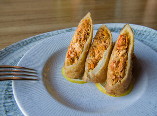 Spring rolls stuffed with marlin, on a white plate with a fork on the side