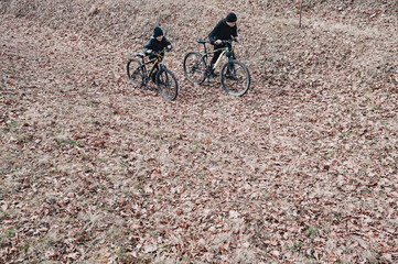Two young people ride mountain bikes along a path covered in fallen autumn leaves. A serene outdoor scene, perfect for leisure and nature imagery.