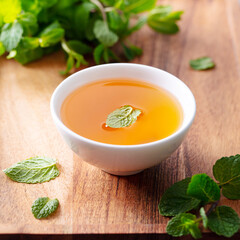Mint tea in a bowl on a wooden tray. Brown background. Close up.