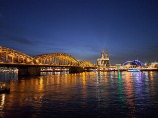 Fototapeta premium die Hohenzollernbrücke in abendlicher Beleuchtung mit Farbspiegelung im Fluss, Köln