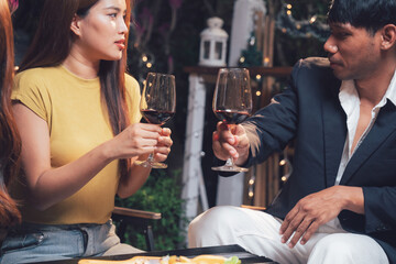 Nighttime Cheers: Friends toast with red wine under fairy lights, enjoying an intimate and stylish evening gathering.  