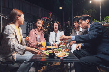 Nighttime Gathering: Friends enjoying a delightful meal together, sharing laughter and conversation under the soft glow of outdoor lights.  
