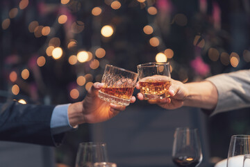 Cheers to Success: Two hands clink glasses of amber liquid in a toast, capturing the celebratory spirit of a successful event or partnership.
