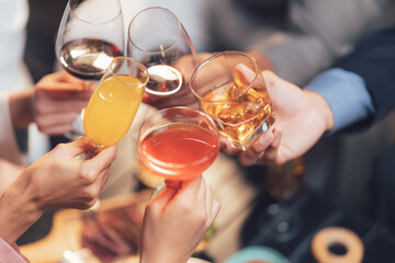 Cheers to Success: A close-up shot of hands clinking glasses filled with various beverages - red...
