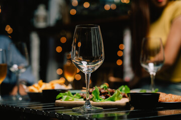 Nighttime Dinner Gathering: A captivating close-up of an empty wine glass at the center of a table laden with delicious food, surrounded by friends enjoying a festive evening under warm.